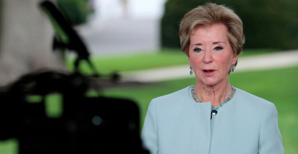 Linda McMahon stands while doing a TV interview and stares directly at a TV camera.