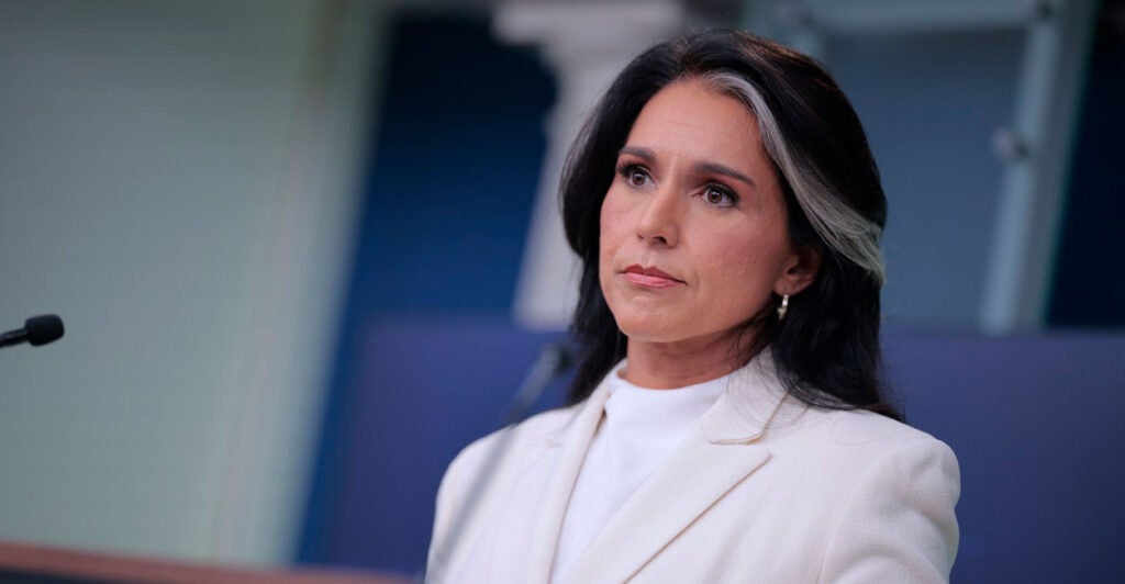 Tulsi Gabbard stands in front of a podium and microphone and stares into the crowd.
