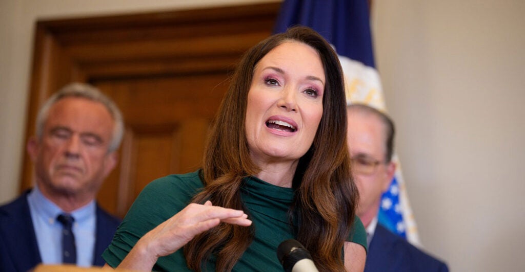 Brooke Rollins stands at a podium in front of microphone and gestures with her right hand as she speaks.