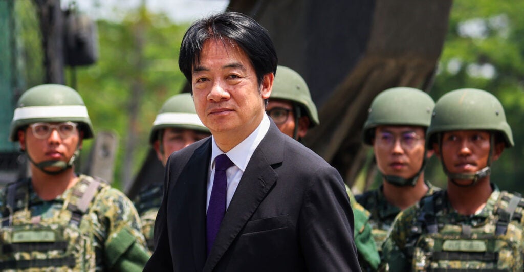 Taiwanese President Lai-Ching Te in black suit, backed by a number of Taiwanese soldiers.