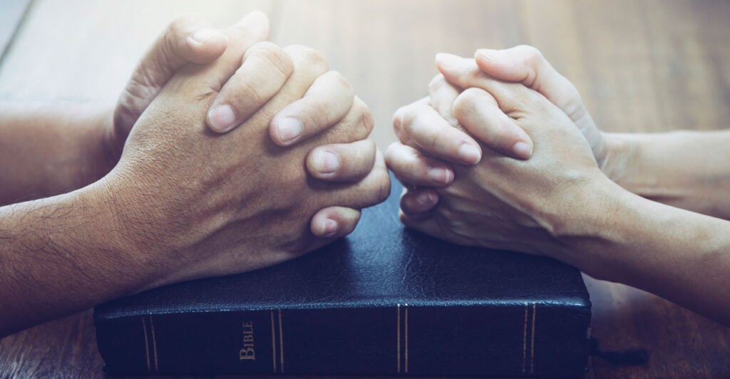 Close-up of male hands and female hands clasped atop a Bible.