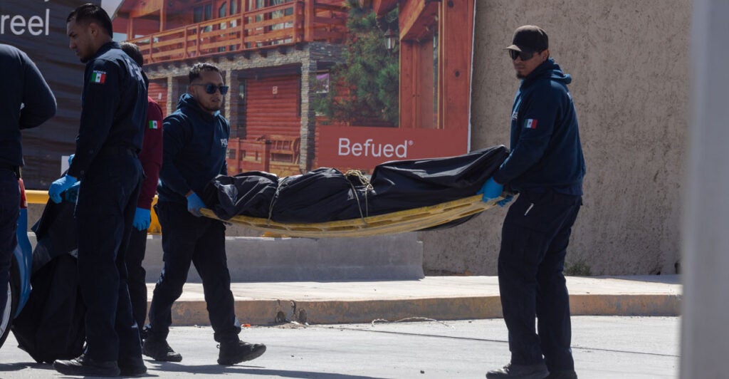 Two Mexican police officers carry the covered body of a murder victim on a stretcher.