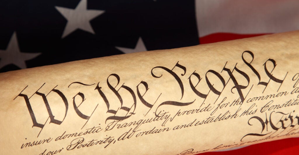 A roll of the U.S. Constitution against a flag backdrop, with "We the People" predominant.