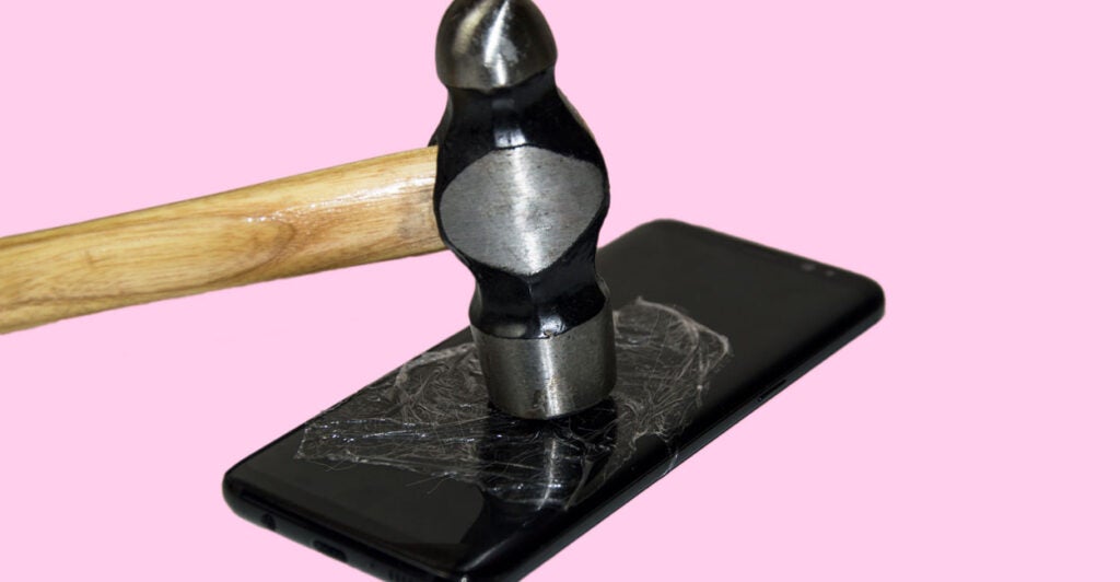 A hammer cracks the screen of a smartphone.