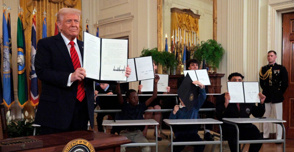 President Trump holds up his executive order reducing the size of the Department of Education. Children behind him also hold up copies of the executive order.