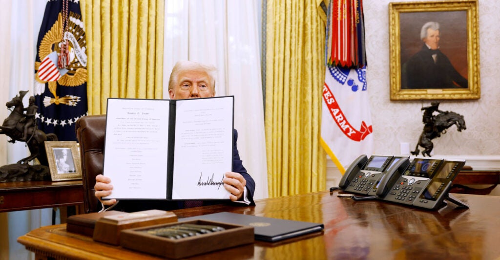 President Donald Trump in Oval Office holds up signed executive order.