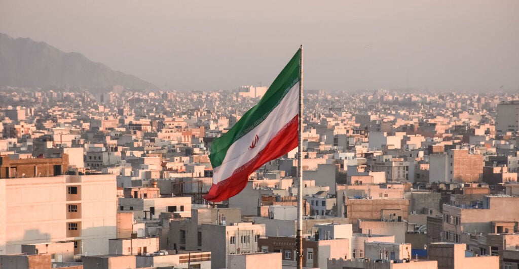 An Iranian flag waves with a cityscape of Tehran, Iran, as backdrop.