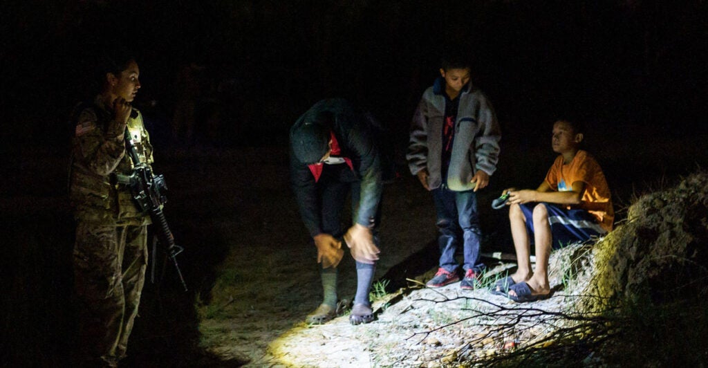 A National Guardswoman speaks to three unaccompanied children at night on the banks of the Rio Grande in Roma, Texas, on July 9, 2021.