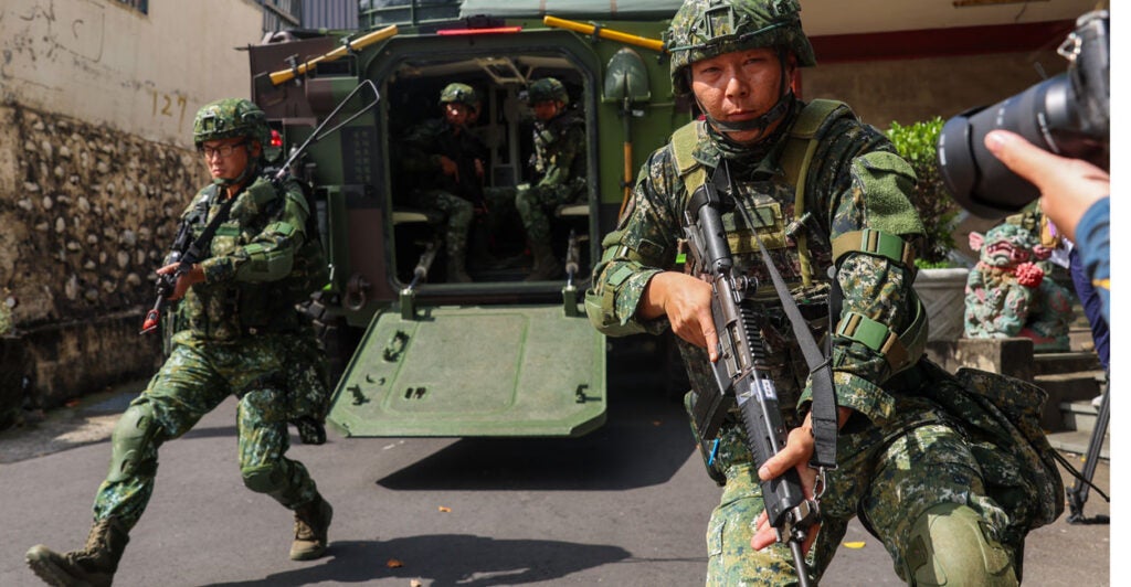 Armed Taiwanese soldiers emerge from an armored vehicle on a street.