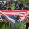 "No Kings" protesters square off against police officers. Man holds upside down American flag in their face.