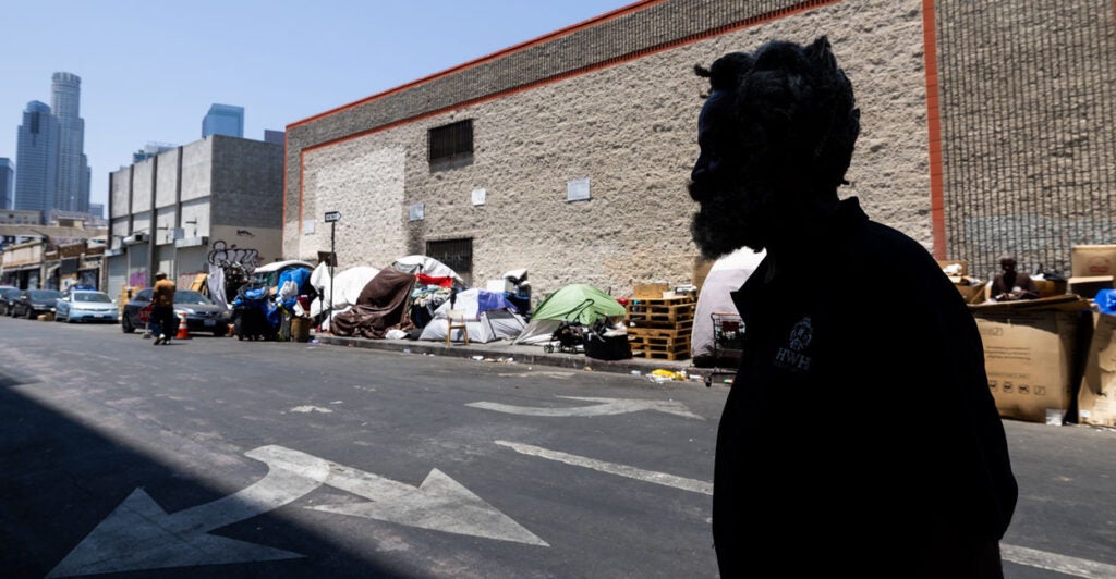 Homeless man in silhouette with Skid Row in background.