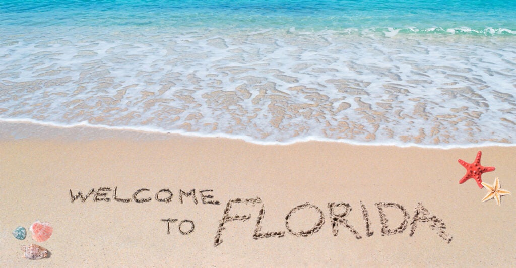 A beautiful beach with turquois water and "Welcome to Florida" written in the sand.