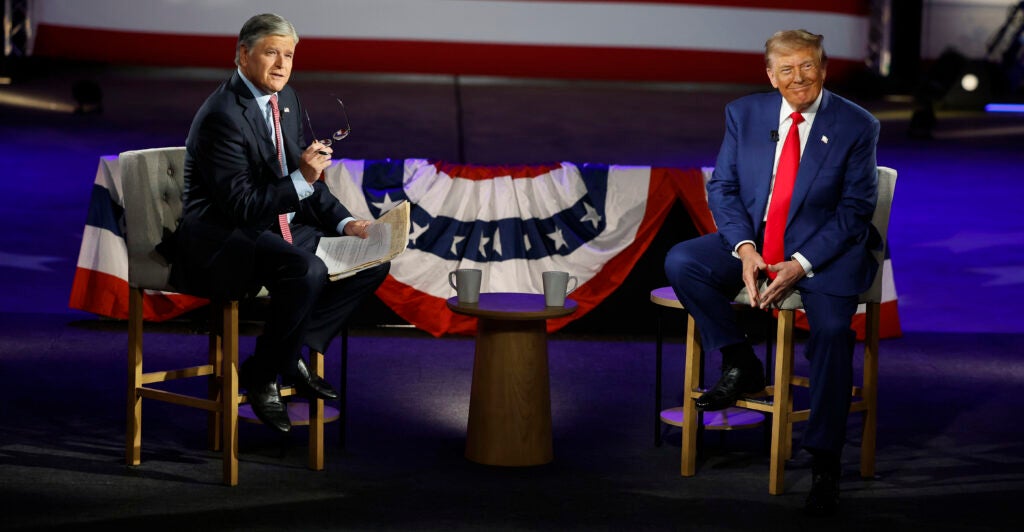 Donald Trump and Fox News host Sean Hannity sit in chairs in front of flag bunting during a 2024 town hall.