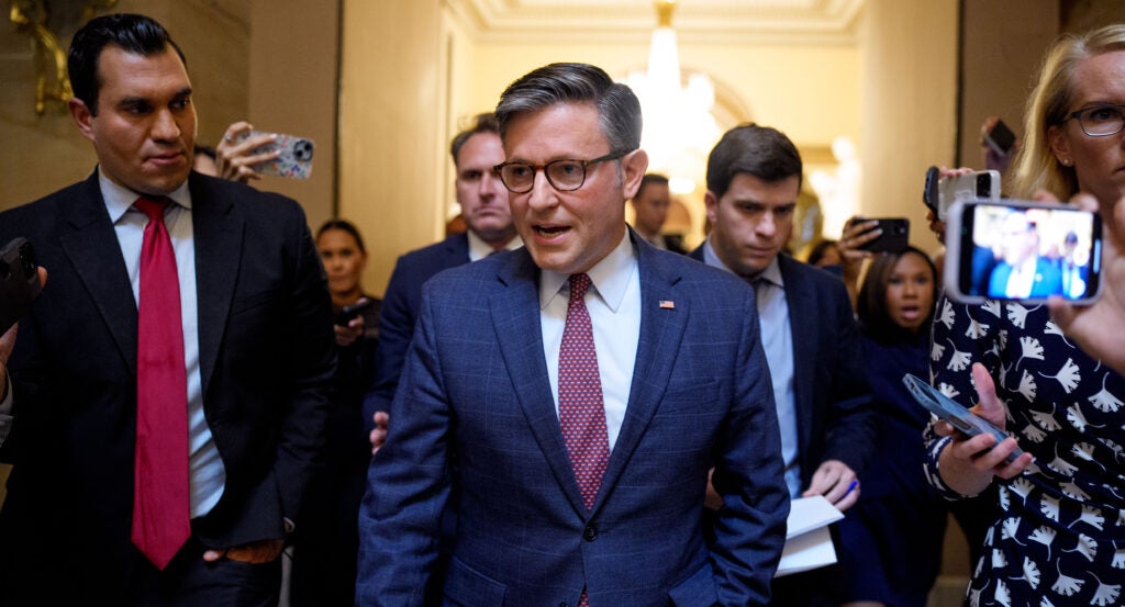 House Speaker Mike Johnson speaks while walking toward the camera, followed by members of both Congress and press.