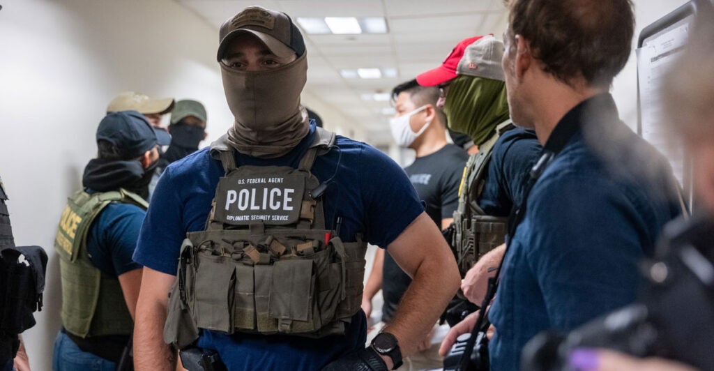 A masked federal agent stands in a courthouse hallway.
