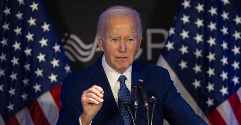 Joe Biden in a blue suit in front of two American flags