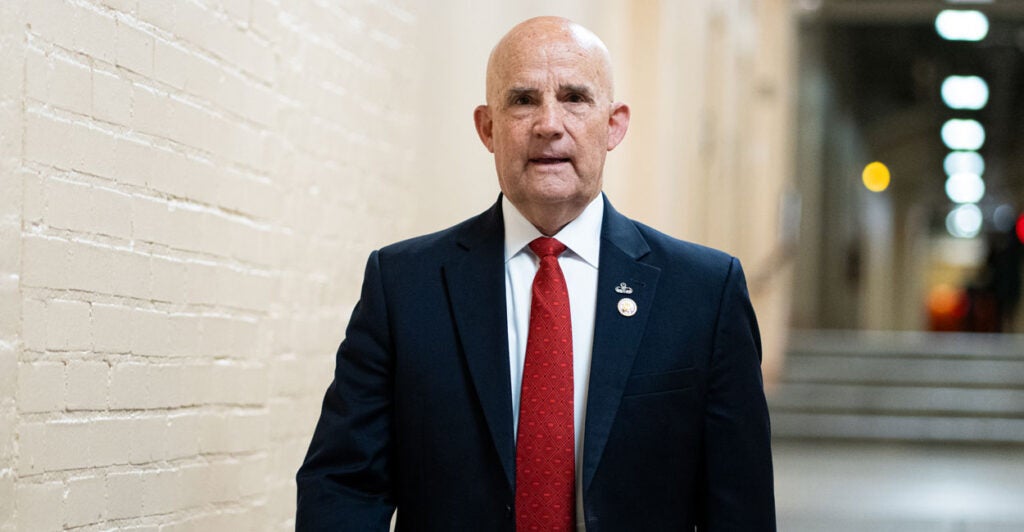 Rep. Keith Self in a blue suit with red tie walks down a hallway.