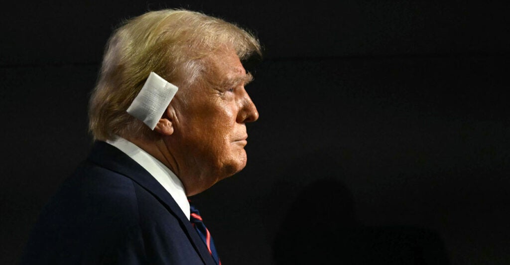 A profile photo of Donald Trump in front of a black background shows his bandaged ear.