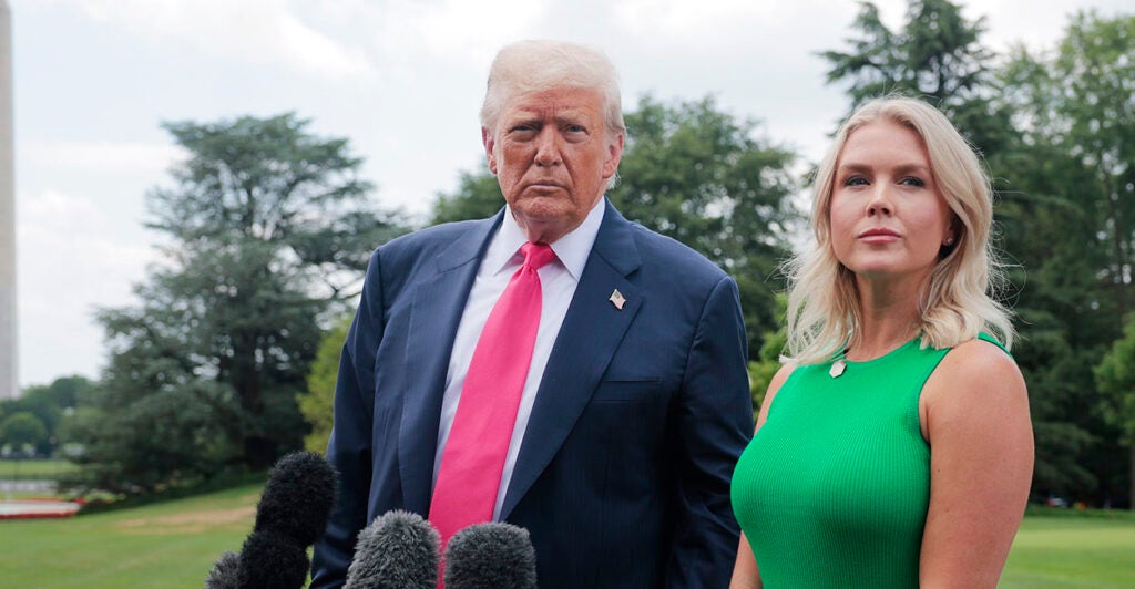 Donald Trump in a blue suit stands next to Karoline Leavitt in a green dress