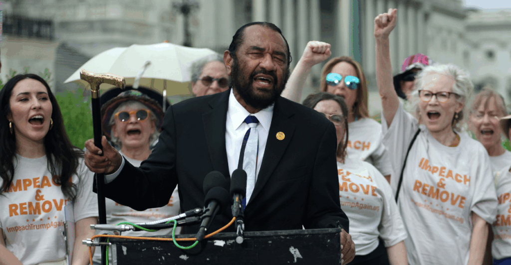 Rep. Al Green stands at a podium outside the U.S. Capitol wearing a dark suit and a white tie and holding up a gold-headed cane as he speaks into a microphone at a rally