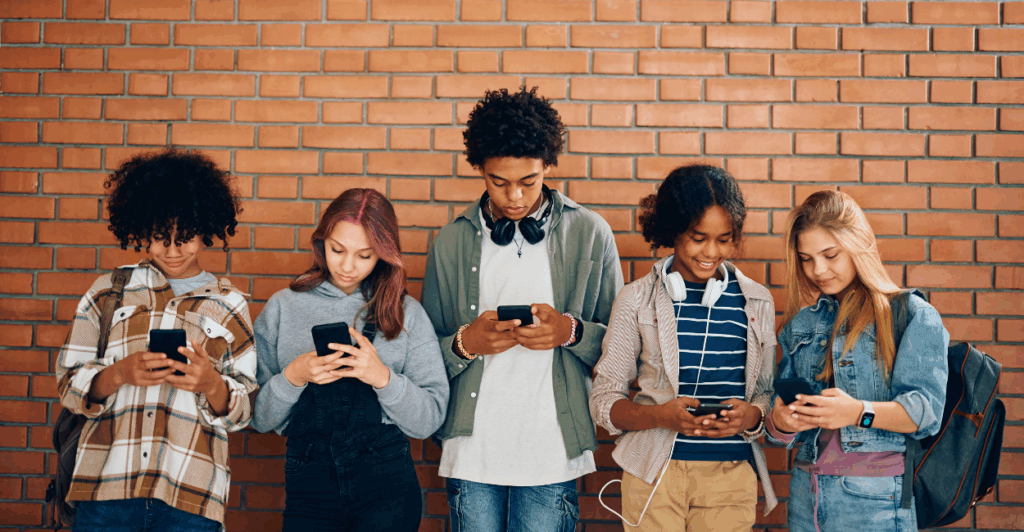 A group of kids stand in front of a brick wall looking at their phones