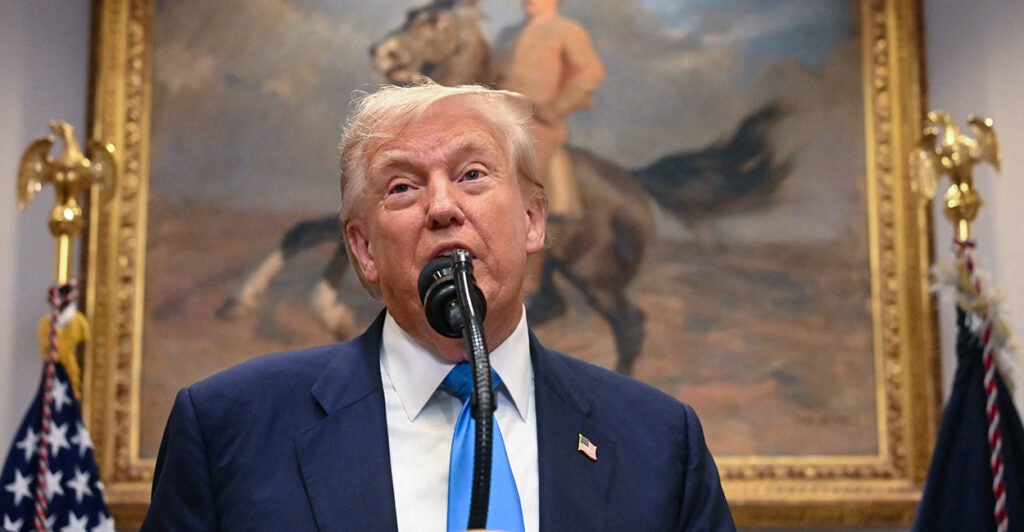 President Donald Trump with a portrait of Teddy Roosevelt on a horse on the wall behind him.