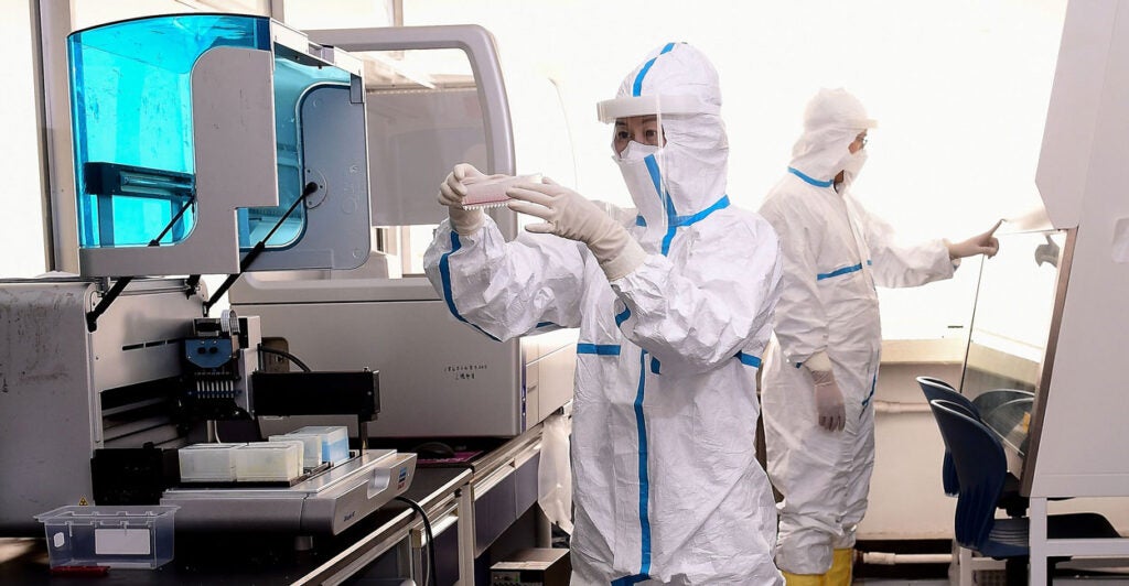 Lab technicians in China in biohazard suits work in a laboratory reviewing samples