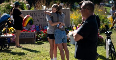 Two teen girls hug in front of a memorial of flowers at Annunciation Catholic Church.