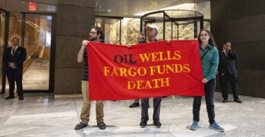 Protesters hold up a sign that says that oil wells and Wells Fargo bank lead to death.