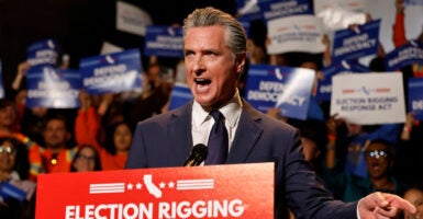 Gavin Newsom stands behind a podium and a microphone as he gives a speech and gestures with his left hand.