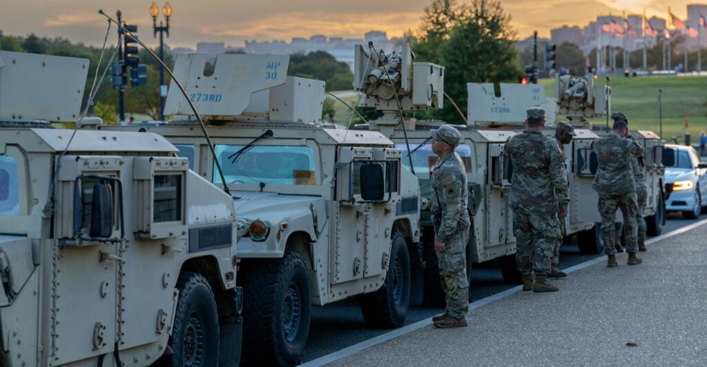 Several armored vehicles are parked along a street in Washington D.C. with National Guard troops standing by them.