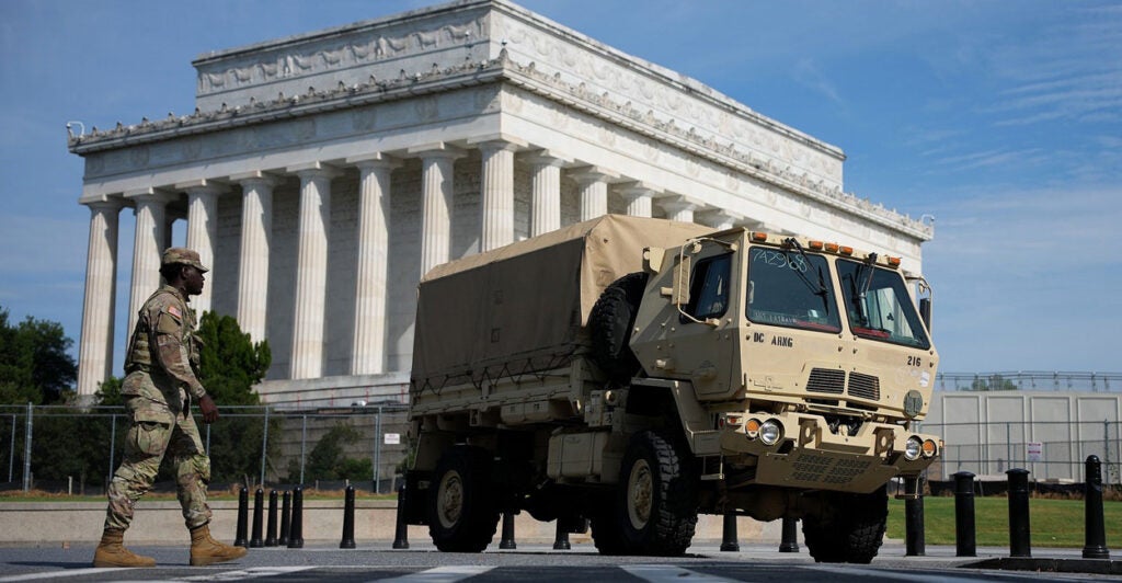 A National Guard member walks to an armored vehicle with the Lincoln Memorial in the background.