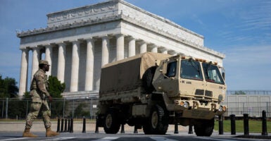A National Guard member walks to an armored vehicle with the Lincoln Memorial in the background.