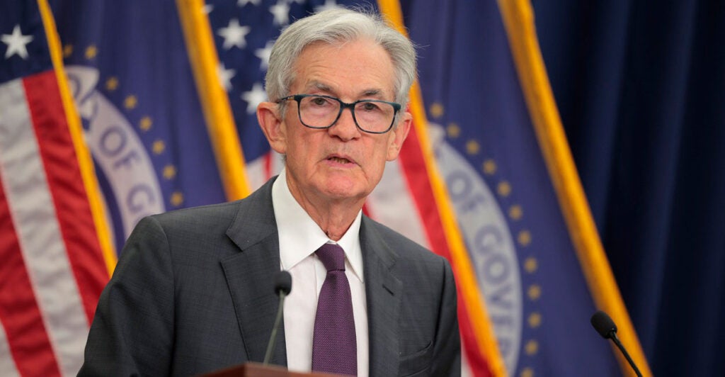 Jerome Powell looks to his left as he stands behind a podium at a press conference.