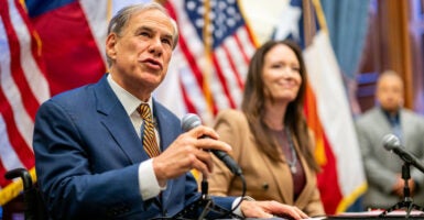 Greg Abbott holds a microphone with his right hand as he speaks during a press conference.