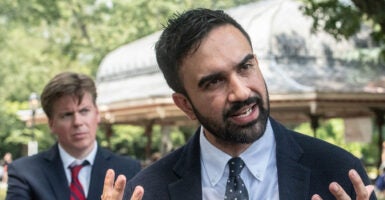 Zohran Mamdani tilts his head to the right and gestures with his hands as he talks to a reporter.