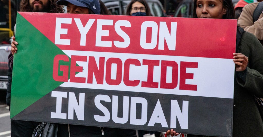 Two people hold up a sign that says, "Eyes on genocide in Sudan."