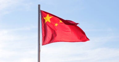 The Chinese flag blows in the wind with blue skies in the background.
