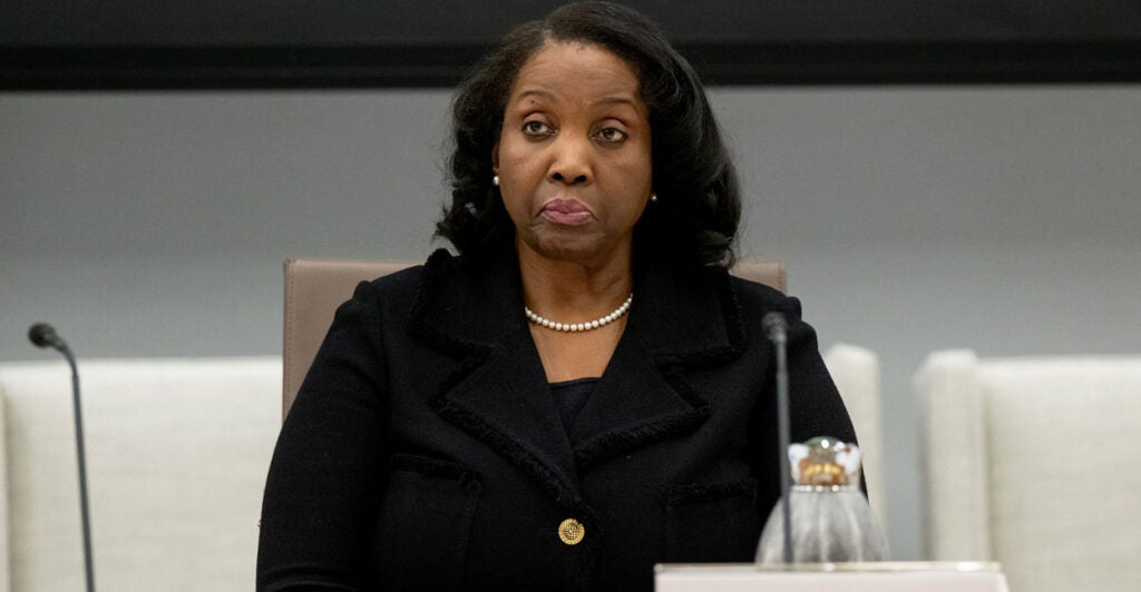 Lisa Cook sits at a table during a meeting with a microphone in front of her and stares to her right.