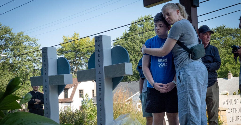 A woman hugs a child as they look upon two crosses marking the sight of a school shooting.