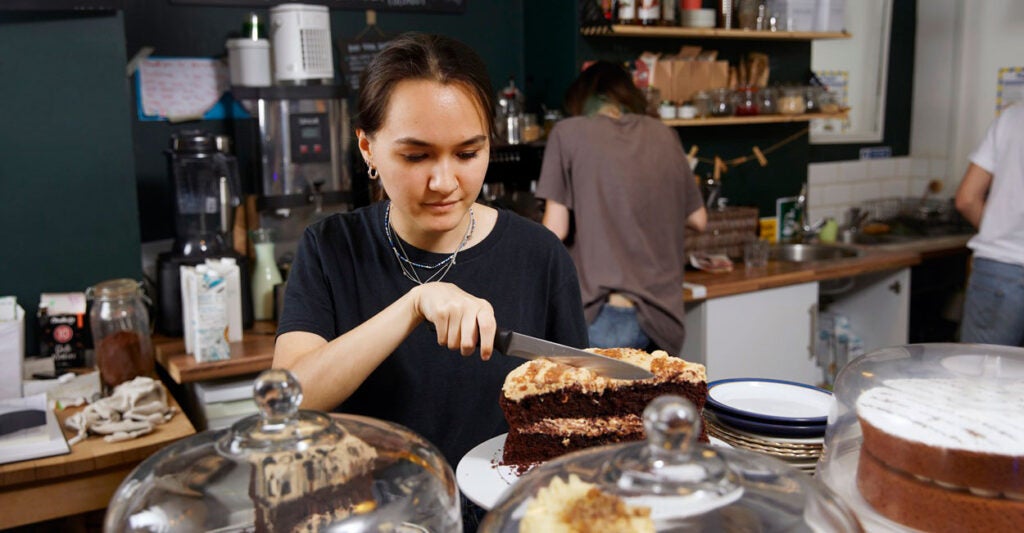 A waitress cuts a piece of cake at a restaurant.