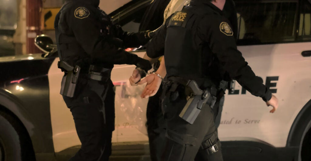 Cops with backs to the camera lead away a suspect.