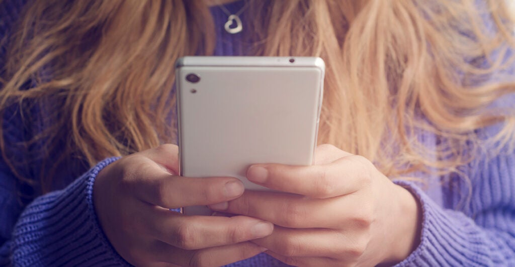 A woman in a purple sweater holds a while cell phone.