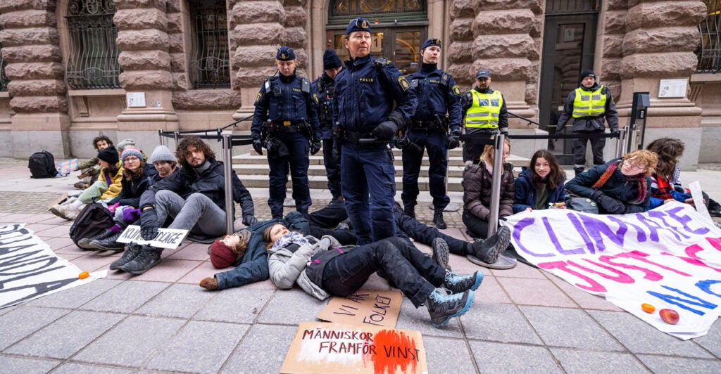 A group of climate protestors sit on the ground, with Greta Thunberg laying on the ground at the feet of several officers.