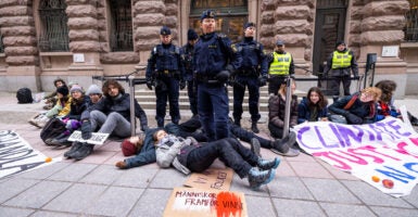 A group of climate protestors sit on the ground, with Greta Thunberg laying on the ground at the feet of several officers.