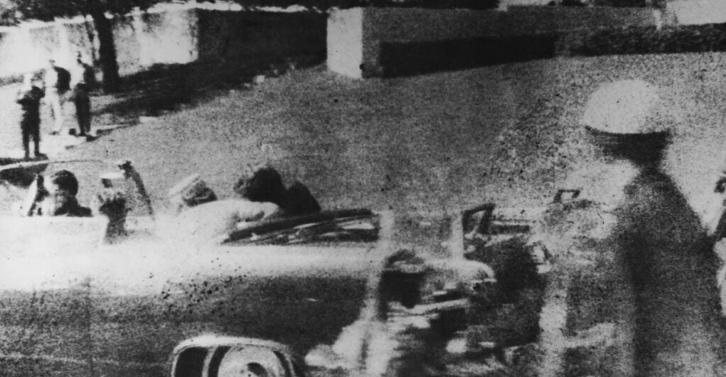 President Kennedy's limosine speeds away after the president was shot. Grassy knoll is in the background.