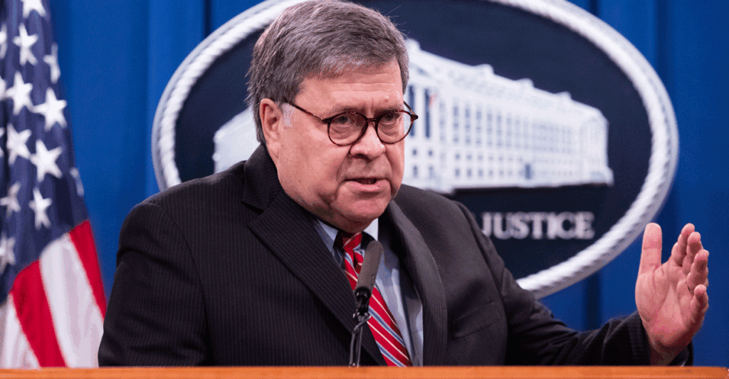 Former Attorney General William Barr stands at a podium in the press room at the Justice Department with a flag and the department seal in the background