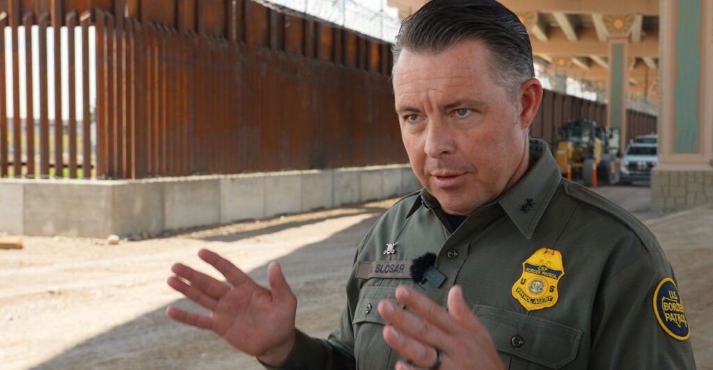 Interim Border Patrol Chief for the El Paso Sector Walter Slosar stands in his green uniform near the border wall.