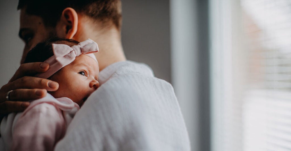 Profile of father holding infant girl dressed in pink.