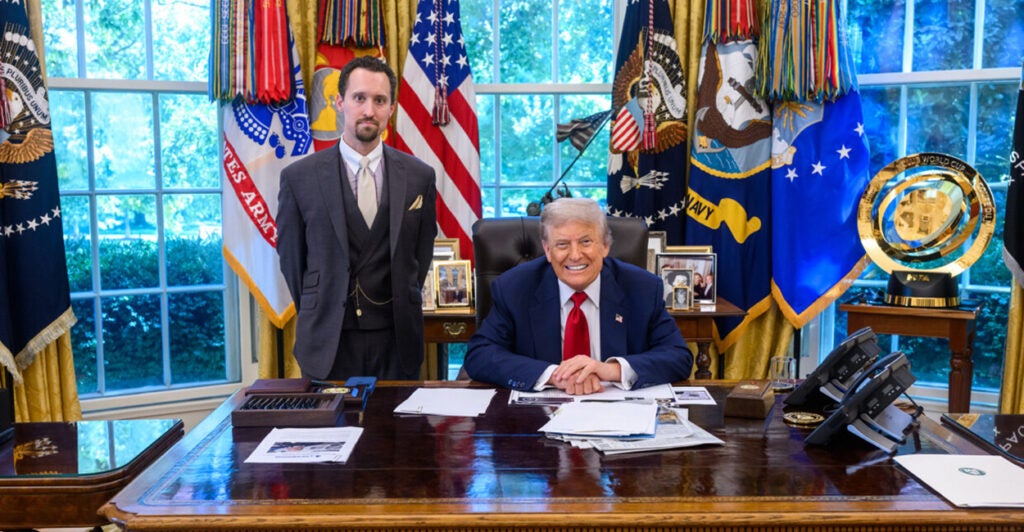 E.J. Antoni stands next to a seated President Trump behind the president's Oval Office desk.
